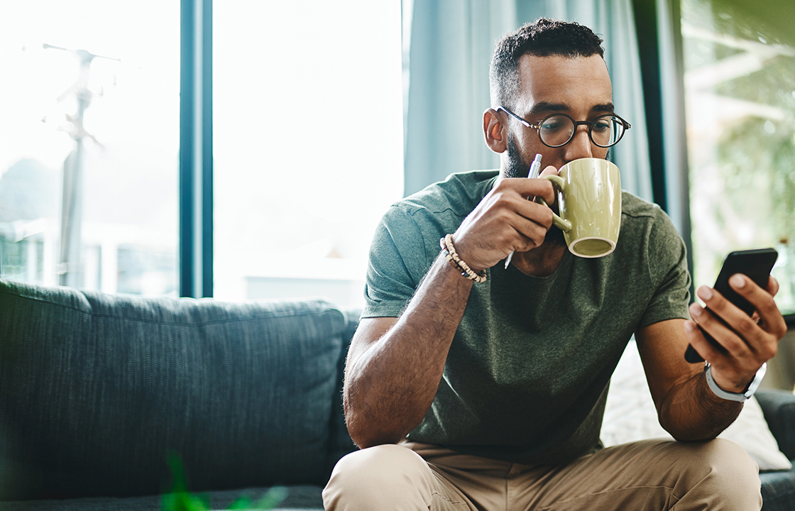 man sitting on the couch drinking a coffee and looking at his phone